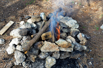 Fireplace in the forest. Smoking campfire on the nature. Camping place with wooden benches in summer forest. Campsite with campfire. Grey and brown big stones and wood for a bonfire in a fireplace