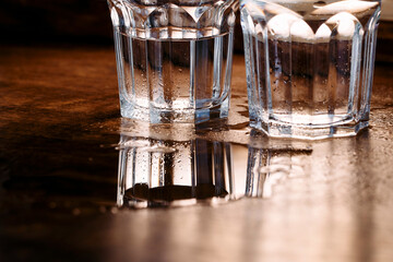 An empty and a half-full glass are reflected in a puddle of water on a table
