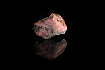 Natural mineral rock specimen - rough rhodonite stone from M. Sidelnikovo, Ural, Russia on black glass background.