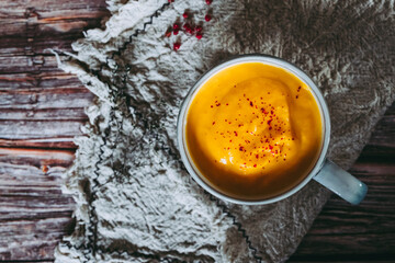Soupe de courge et carottes aux baies roses dans un bol sur une table de cuisine en bois