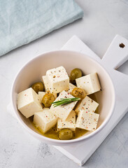 Feta cheese cubes with rosemary and olives in bowl on white background. Organic cheese concept.