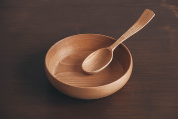 Empty wooden bowl and wooden spoon on a brown table background. Copy, empty space for text