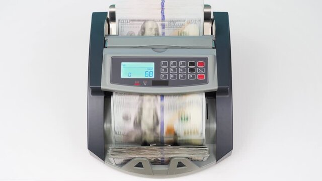 Currency counting money machine counts 100 dollars bills or USD banknotes. Cash bill counter machine stands on white table in bank branch. Automatic mechanism for bank financial operations