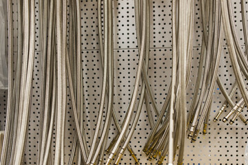 Closed up braided stainless steel texture of flexible hose arranged in a row against white wall.