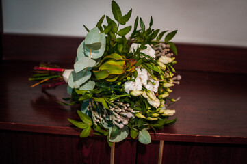 Bridal bouquet with white flowers and green branches on brown background