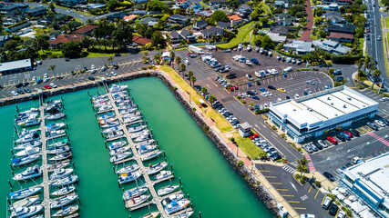 Aerial view on a marina with boat and yachts resting on calm water and cars parked along the shore on a busy plaza. Auckland, New Zealand.