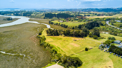 Aerial view of a small river running to the sea through green countryside spotted with little farms. Auckland, New Zealand.