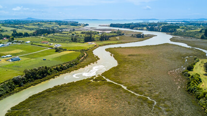 Fototapeta na wymiar Aerial view of a small river running to the sea through green countryside spotted with little farms. Auckland, New Zealand.