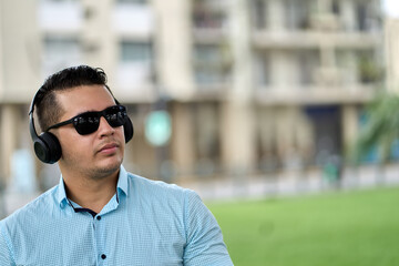 young handsome ecuadorian listening to music with headphones and sunglasses in a park in guayaquil