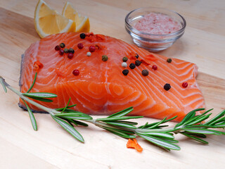 Close-up of slice of red fresh raw salmon fillet with pepper and spices and rosemary next to it. lie on a wooden cutting board. Healthy food concept