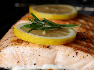 Close-up of ready-made salmon fillet with two lemons and rosemary, salmon in the oven. Healthy food concept