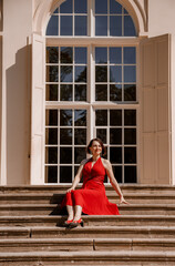 The Great Orangery a classicistic orangery in Lazienki Krolewskie park in Warsaw, Poland. Woman Outdoor Beauty Portrait. A woman with red dress sitting Stairs.