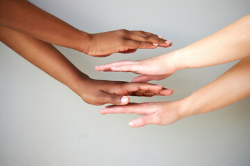 outstretched two diverse female hands holding on top of each other, women keeping empty palm on gray isolated background. people diversity, help, support, love concept