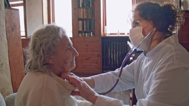 Female doctor use stethoscope to listen heart of elderly woman patient. Nurse home visit, checking health of old senior woman during coronavirus, covid-19 quarantine, self isolation