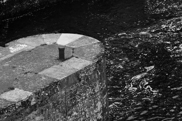 La fin d´un quai en pierre avec une bitte d´amarrage et la rivière qui coule. Photographie...