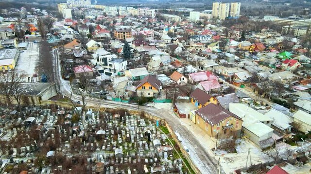 Aerial drone view of a residential distict in Chisinau, Moldova. Multiple buildings, road, cemetery on the left, Cloudy weather, bare trees, winter