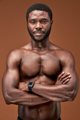 Fototapeta na wymiar black sportsman standing with crossed arms confidently posing at camera, isolated on brown background. sport and bodybuilding concept