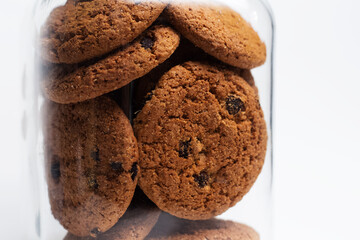Close-up of oat cookies on glass jar on white background.