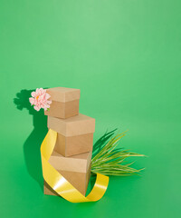 Spring bursting out of  three cardboard boxes layed on top of each other on a green background. Grass, flower and a yellow ribbon bathing in sunlight. Conceptual spring composition, top view.