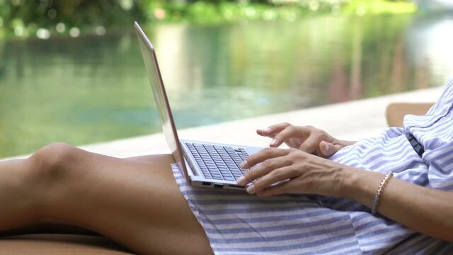 Woman working on laptop sitting by the swimming pool