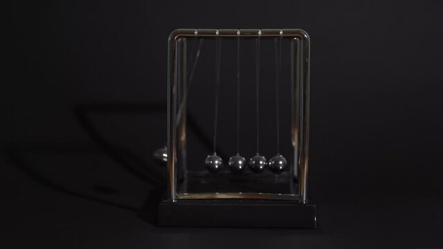 Hand starts the balls motion of Newton's cradle on black background, business concept.