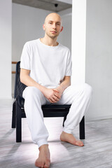 Fototapeta premium calm male sitting in chair in studio and looking at camera, after yoga class, in white clothing. sport, yoga, healthy lifestyle concept. portrait