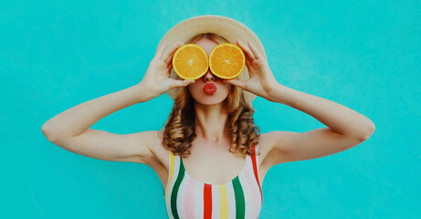 Summer portrait of funny woman covering her eyes with two slices of orange on a colorful blue background