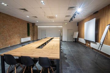 Interior of empty conference hall with black chairs, wooden tables placed as boardroom