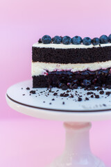 Chocolate sponge cake with a layer of cheese cream. Decorated with blueberries. Delicious wedding cake. Cake on a pink isolated background.