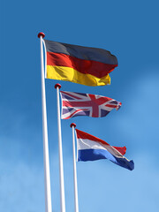 Flags of Germany, United Kingdom and France on flagpoles. Flag of Germany is on top.  Blue sky background.