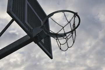 Street basketball hoop with metal chains, close up, cloudy sky in background - 414550164