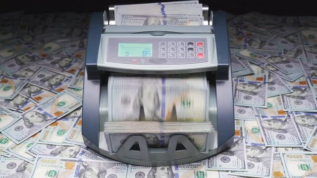 Cash counter money machine counts 100 dollar bills or USD banknotes. Currency counting machine stands on scattered hundred dollars. Automatic mechanism for bank financial operations. Finance concept