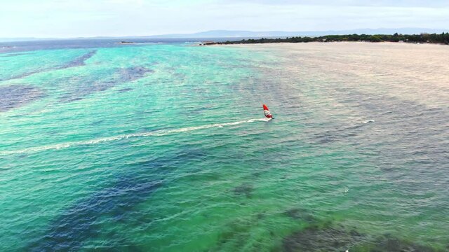 Aerial drone view of a man at windsurfing in Aegean sea. Transparent water, land with greenery in Greece