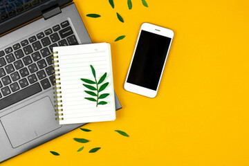 Freelancer workspace with laptop, notepad and smartphone, spring green leaves on a yellow background, copy space