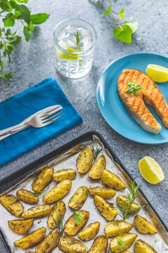 Baked potatoes on tray and grilled salmon steak with basil served with gin and tonic with lime and rosemary on light gray table surface