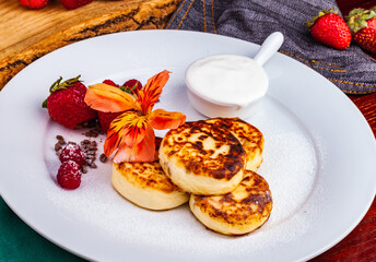 Breakfast. Cottage cheese pancakes, syrniki, curd fritters with fresh berries raspberry and strawberry, sour cream on white plate. Russian or Ukrainian cuisine.