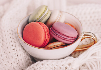 Sweet dessert, macaroons in golden mug on white wool background, morning breakfast