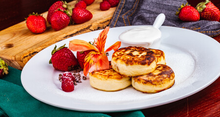 Breakfast. Cottage cheese pancakes, syrniki, curd fritters with fresh berries raspberry and strawberry, sour cream on white plate. Russian or Ukrainian cuisine.