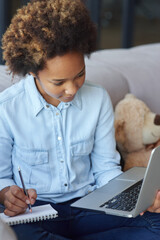 Get new knowledge. Focused teen schoolgirl using laptop, making notes during online lesson while sitting on the couch at home