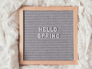 Top view on grey letter board with season greeting HELLO SPRING. Crumpled white laces. Signs on textile background.