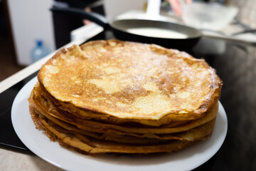 a stack of pancakes on a white plate on a kitchen background