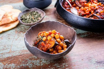 Modern style slow cooked Lebanese vegetarian eggplant stew maghmour served with chickpeas and pita bread as close-up in a rustic design bowl