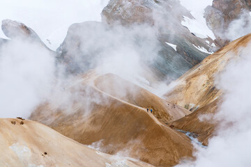 Iceland, Southern Highlands, Kerlingarfjoll Mountains. Two hikers climbing the stairs to the trail over the red volcanic rhyolite stone and through the steam of the thermals.
