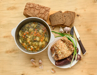 baked meat, soup and blood sausage on a plate, green onion and garlic on wooden background, home...