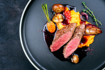 Modern style traditional wild hare back filet braised with wild berries and red wine jus with mashed carrot puree and sweet potato served as top view on Nordic design plate with copy space left © HLPhoto