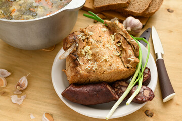 baked meat, soup and blood sausage on a plate, green onion and garlic on wooden background, home cooking