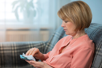 Woman is disinfecting her cell mobile phone at home, wipes smartphone with a napkin to remove coronavirus covid-19 bacterias. Hygiene of gadgets, devices. 