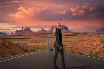 Blonde caucasian woman standing on iconic road in Utah Arizona desert Monument Valley with pink,...