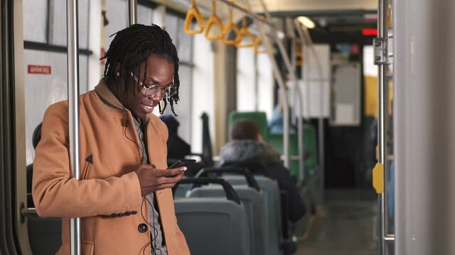 Young african american man use smartphone sitting in tram traffic typing at sunny day handsome passangers stylish transportation using way internet online texting portrait guy slow motion.