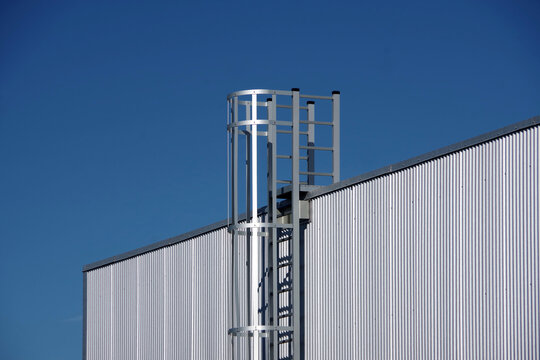 Segment of an industrial warehouse building with corrugated metal siding and a stainless steel access ladder to the roof